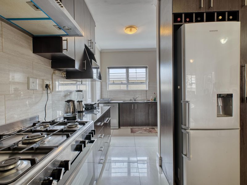 A functional kitchen featuring dark cabinetry, a gas hob with extractor fan, tiled flooring, and a double sink with a window view.
