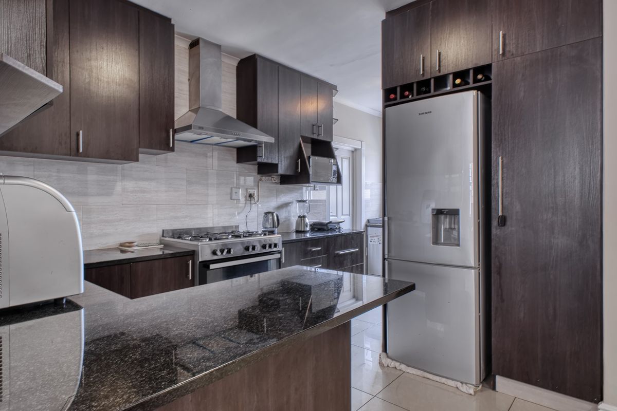 Modern kitchen featuring dark wood cabinetry, granite countertops, a gas stove with extractor fan, and tiled finishes throughout.