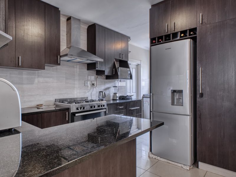 Modern kitchen featuring dark wood cabinetry, granite countertops, a gas stove with extractor fan, and tiled finishes throughout.