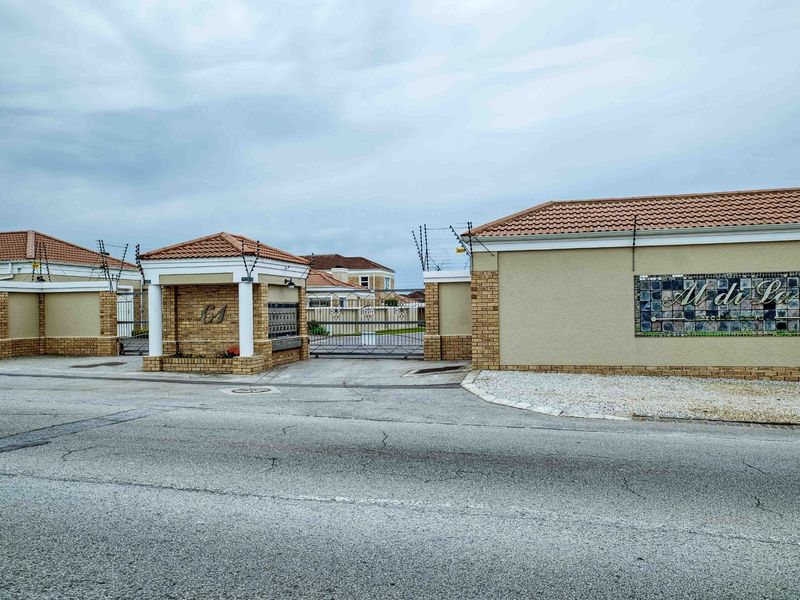 Front entrance view of the townhouse complex featuring a secure gated access point, brick boundary walls, and electric fencing.