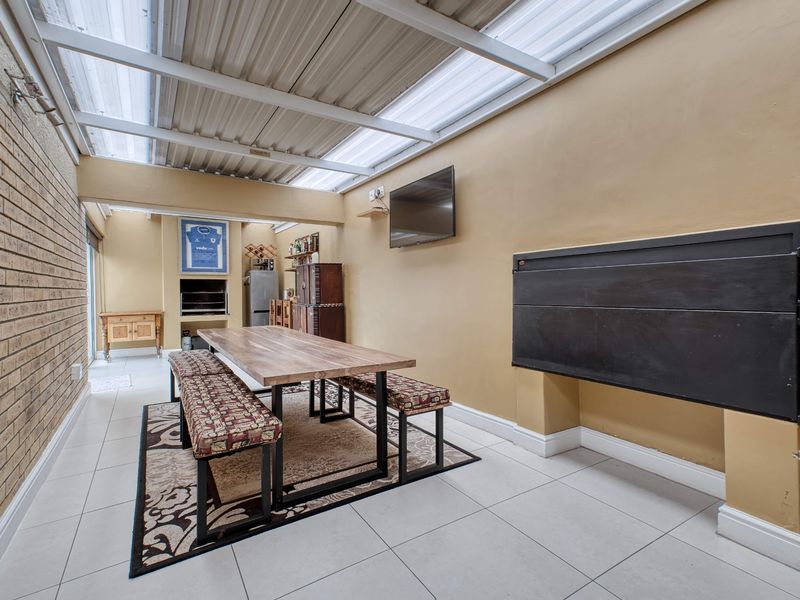 Covered patio area featuring a built-in braai, tiled flooring, and a translucent roof, providing a functional space for outdoor dining and entertainment.