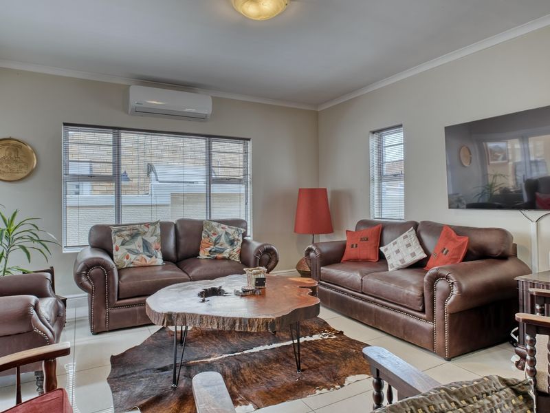 A comfortable living room featuring tiled flooring, a wall-mounted air conditioning unit, and large windows with venetian blinds.