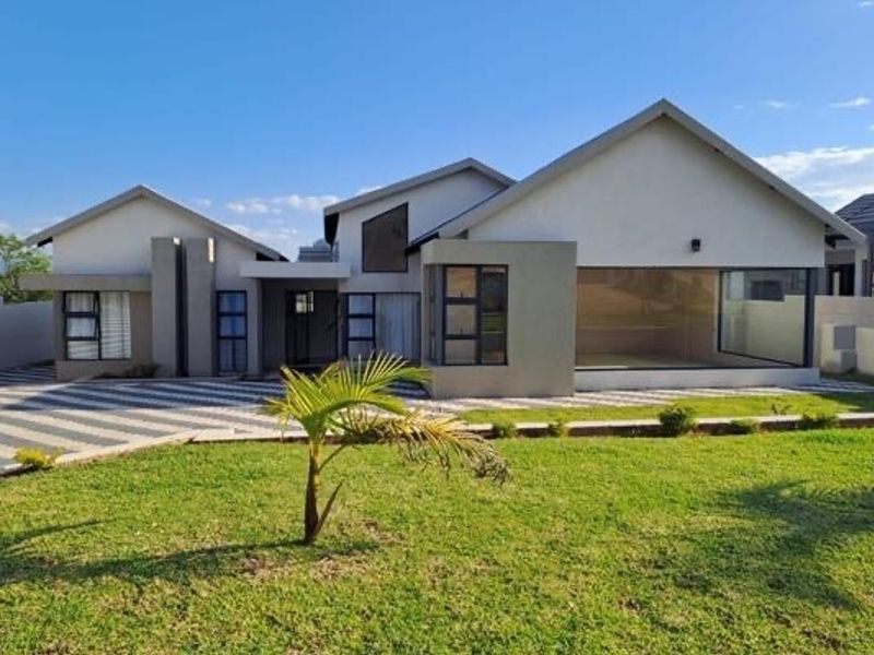 Modern single-story residential home featuring a multi-pitched roof, large aluminium windows, and a spacious paved driveway set within a landscaped garden.