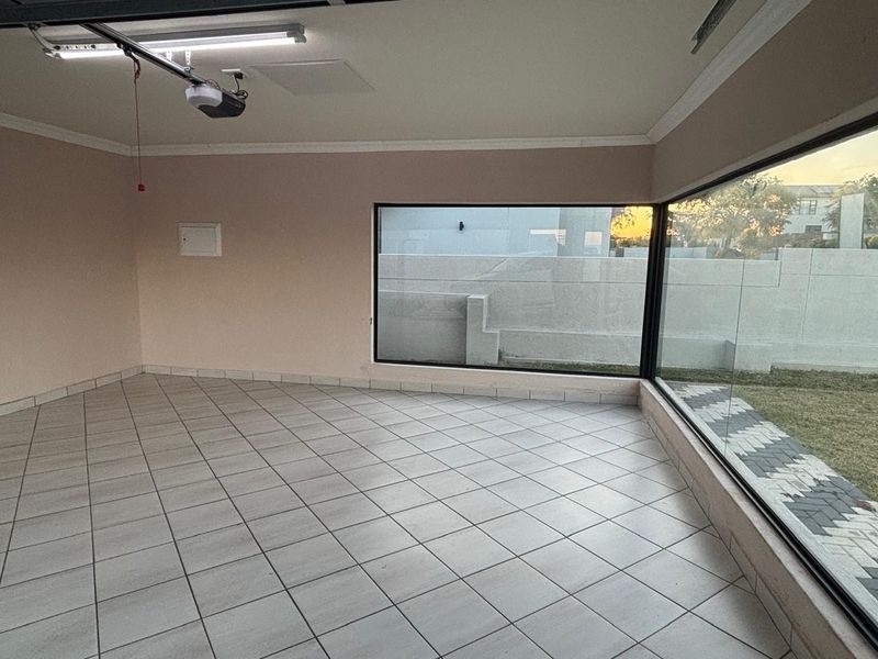 A clean, empty garage space featuring tiled flooring, a garage door motor, and a large corner window providing natural light and garden views.