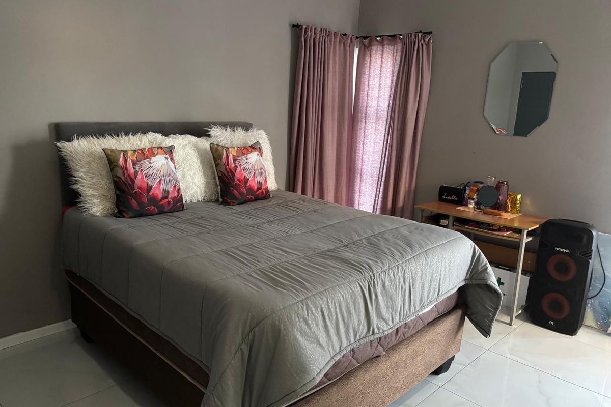 A functional bedroom featuring neutral wall tones, tiled flooring, and window treatments, offering a comfortable and well-maintained living space.