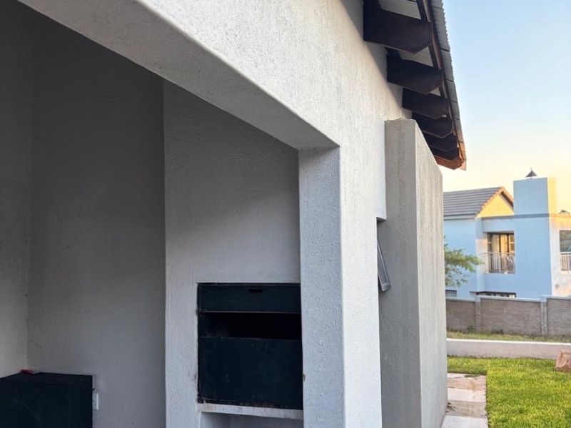 Covered patio area featuring a built-in braai, tiled flooring, and exposed rafters, overlooking the rear garden space.
