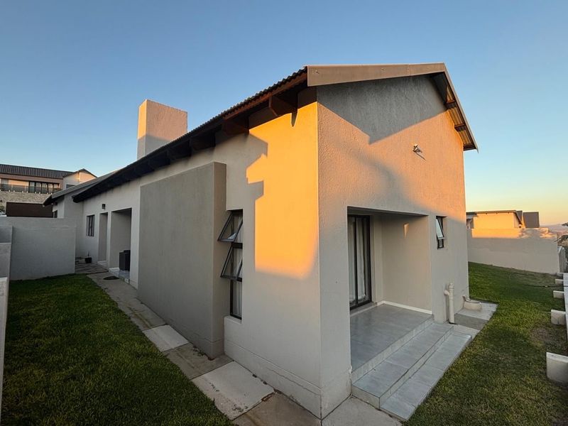 Rear view of the house featuring a tiled patio, sliding glass doors, and a clean plastered facade under a corrugated metal roof.
