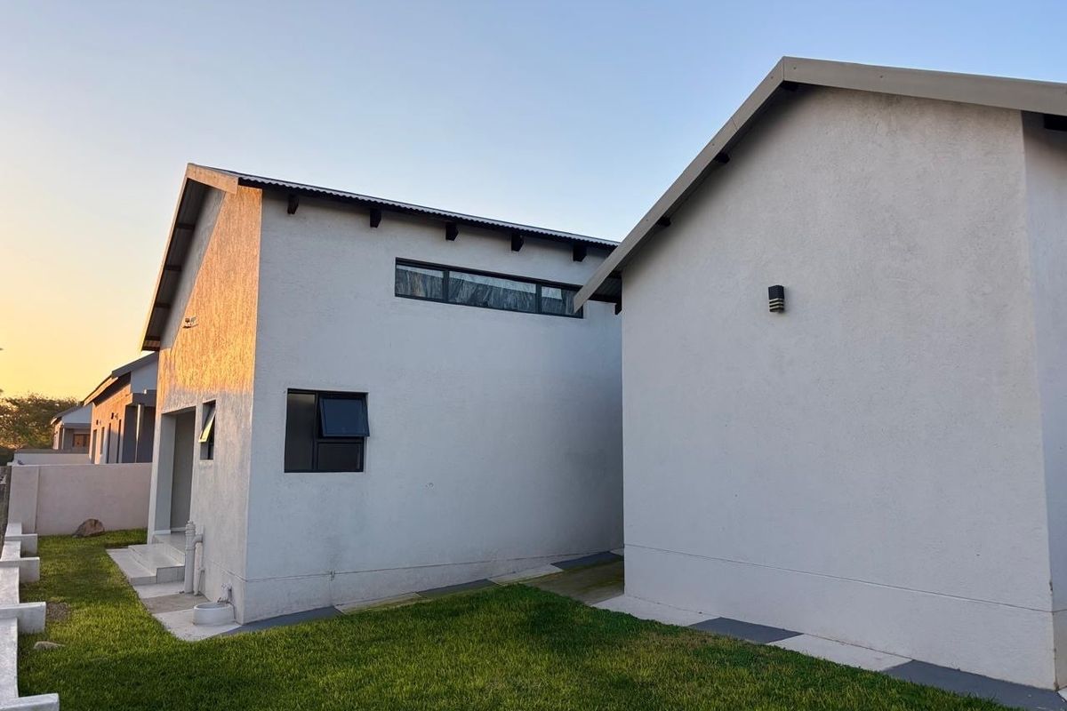 A view of the rear exterior of the house featuring modern white rendered walls, pitched rooflines, and a well-maintained lawn area.
