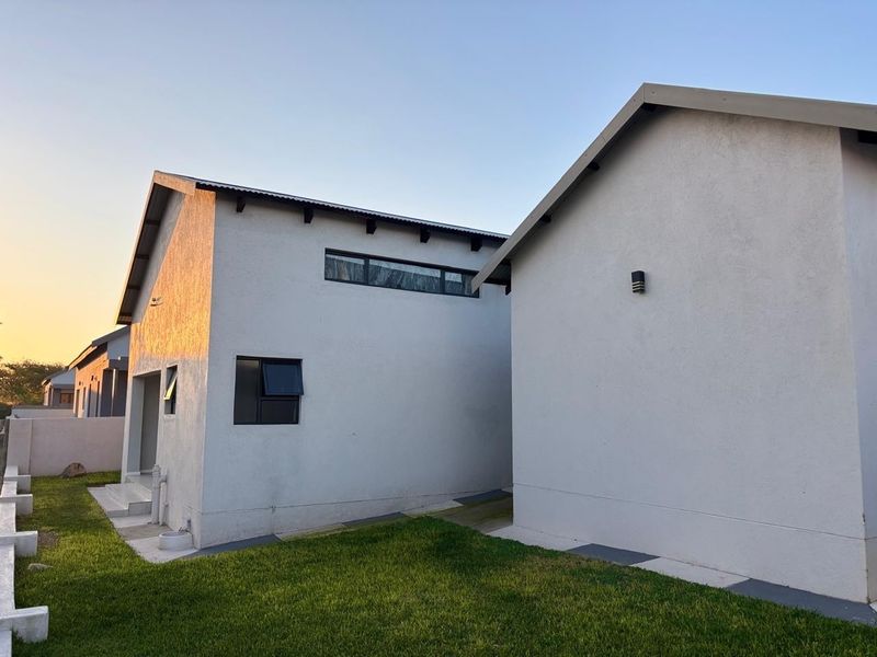 A view of the rear exterior of the house featuring modern white rendered walls, pitched rooflines, and a well-maintained lawn area.