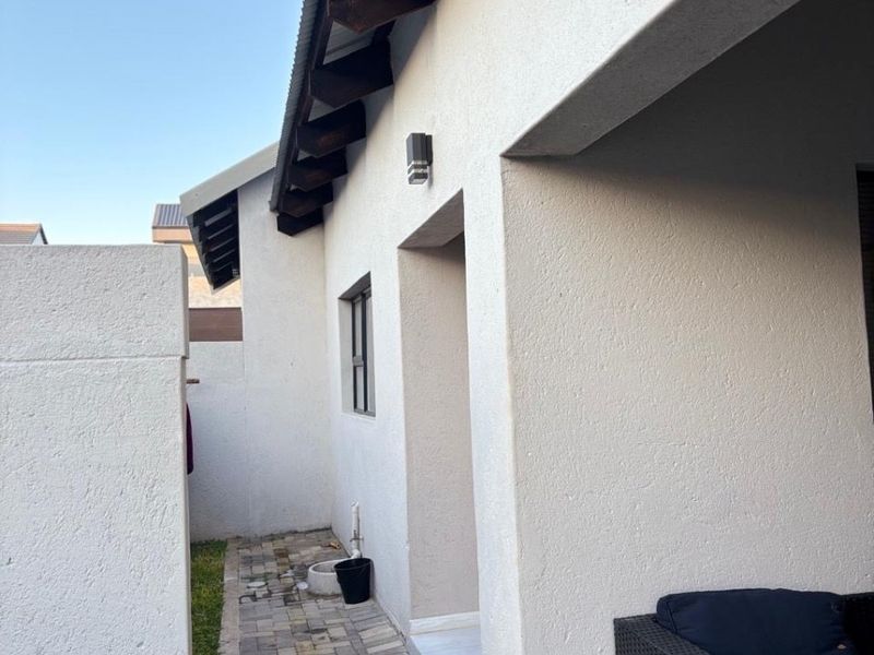 A side view of the property featuring a paved walkway, exposed timber rafters, and a clean exterior wall finish.