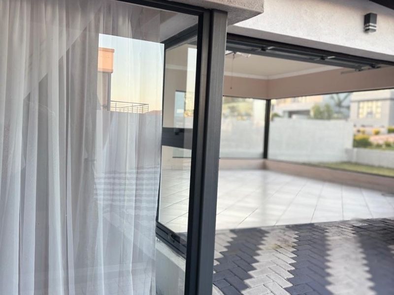 A spacious covered patio area featuring tiled flooring, large sliding glass doors, and a skylight, providing a seamless transition to the outdoor paved space.