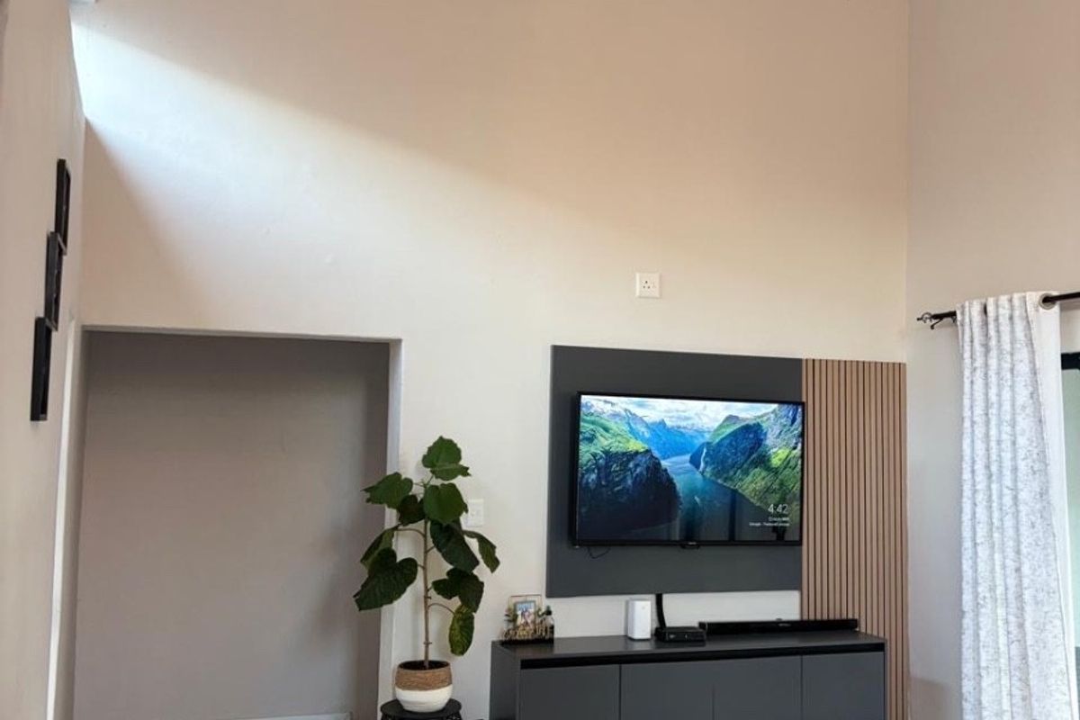 Spacious living room featuring a high vaulted ceiling with exposed beams, tiled flooring, and a modern built-in media wall with timber slat detailing.