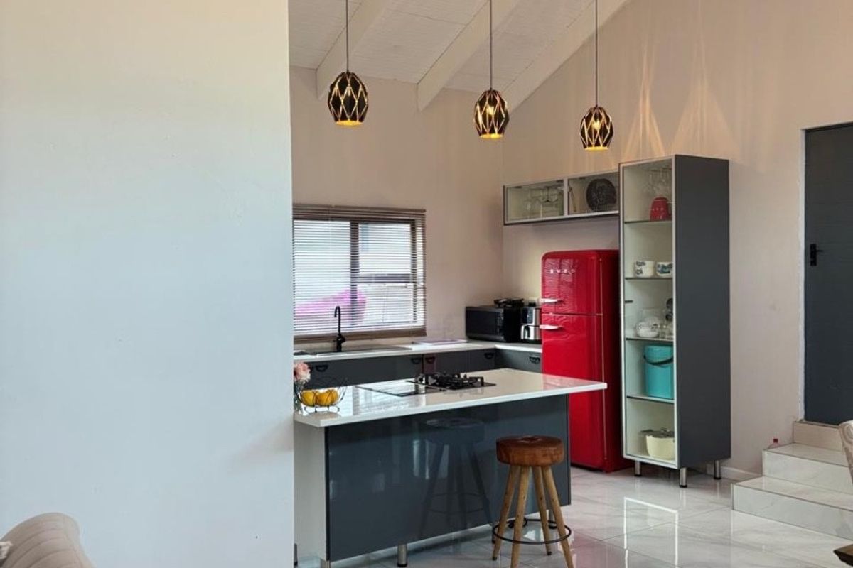 Modern kitchen featuring a central island, sleek cabinetry, vaulted ceilings with pendant lighting, and polished tiled flooring in an open-plan layout.