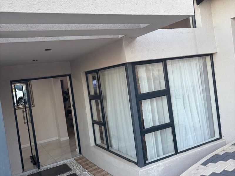 Modern front entrance featuring a covered porch, large aluminium-framed windows, and a clean paved driveway with a stone-accented walkway.
