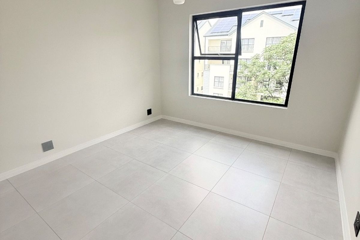 A bright, empty bedroom featuring neutral tiled flooring, clean white walls, and a modern black-framed window with natural light.