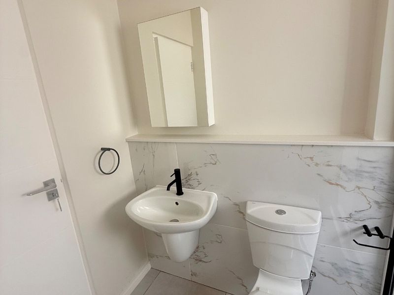 A modern, clean guest bathroom featuring a wall-mounted basin with black fixtures, a toilet, and elegant marble-look wall tiling.
