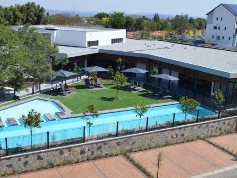 An elevated view of a well-maintained communal pool area featuring a swimming pool, landscaped garden, and paved parking facilities within the apartment complex.