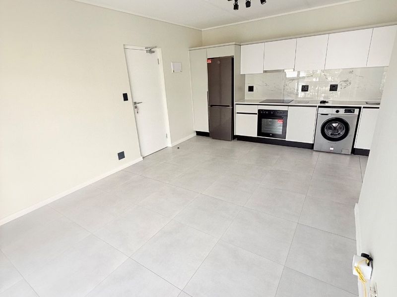 Modern open-plan kitchen featuring sleek white cabinetry, integrated appliances, marble-look splashback, and neutral tiled flooring in a clean, well-maintained space.