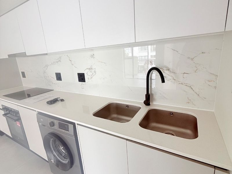 Modern kitchen featuring sleek white cabinetry, stone countertops, marble-look splashback, integrated appliances, and a contemporary black mixer tap.