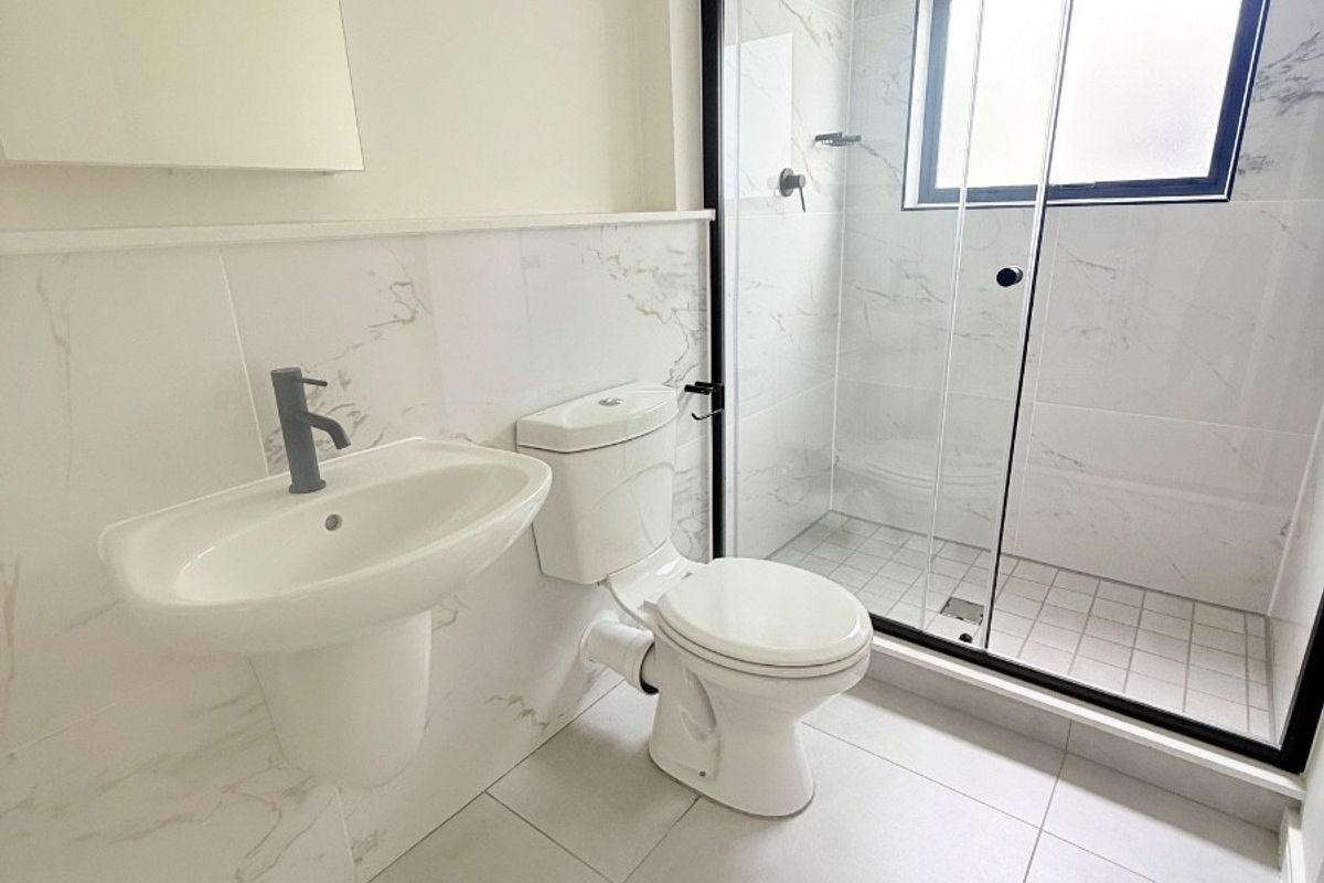 Modern bathroom featuring a wall-mounted basin, toilet, and a walk-in shower with a sleek black-framed glass enclosure and marble-look wall tiling.