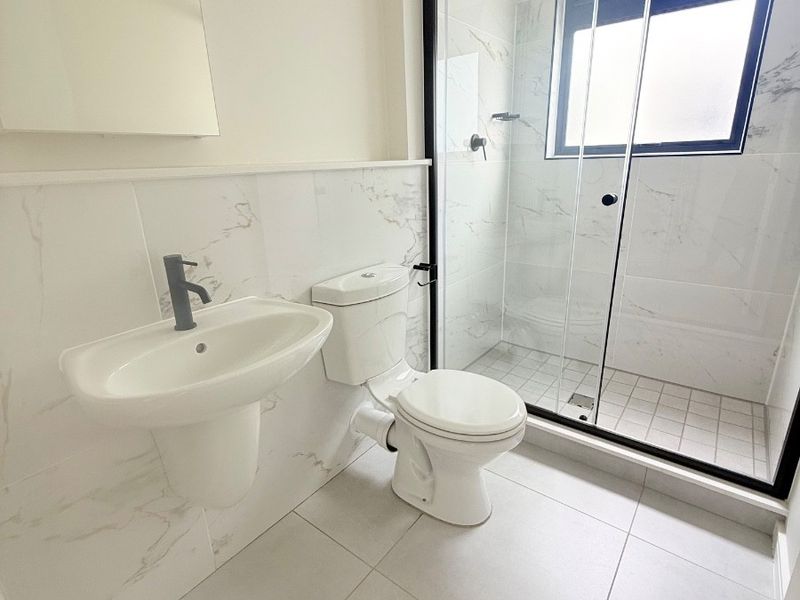 Modern bathroom featuring a wall-mounted basin, toilet, and a walk-in shower with a sleek black-framed glass enclosure and marble-look wall tiling.