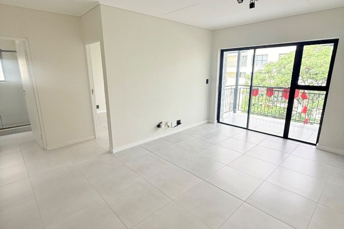 A bright, modern, and empty living room featuring large format floor tiles, track lighting, and a sliding glass door leading to a private balcony.