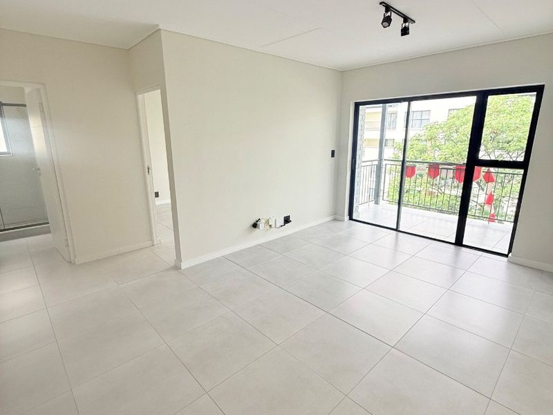 A bright, modern, and empty living room featuring large format floor tiles, track lighting, and a sliding glass door leading to a private balcony.