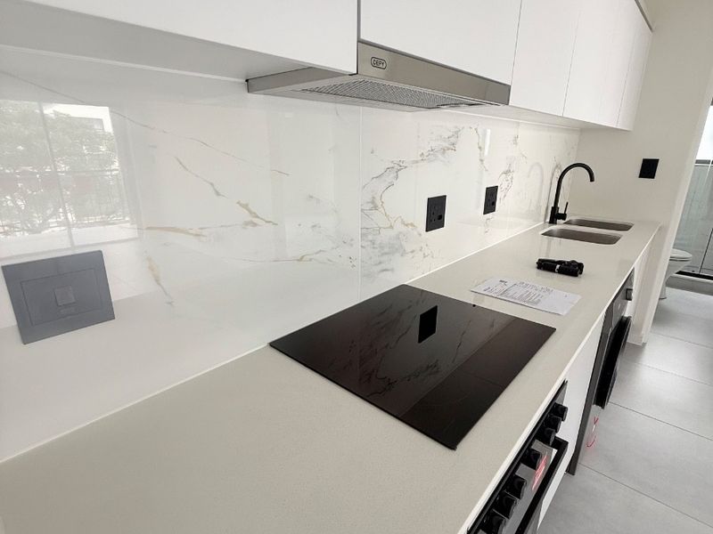 Modern kitchen featuring sleek white cabinetry, stone countertops, marble-look splashback, integrated electric hob, oven, and stainless steel sink with contemporary fixtures.