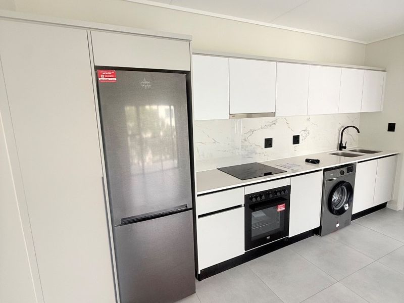 Modern kitchen featuring sleek white cabinetry, stone-look backsplash, integrated oven and hob, and contemporary black fixtures with neutral tiled flooring.