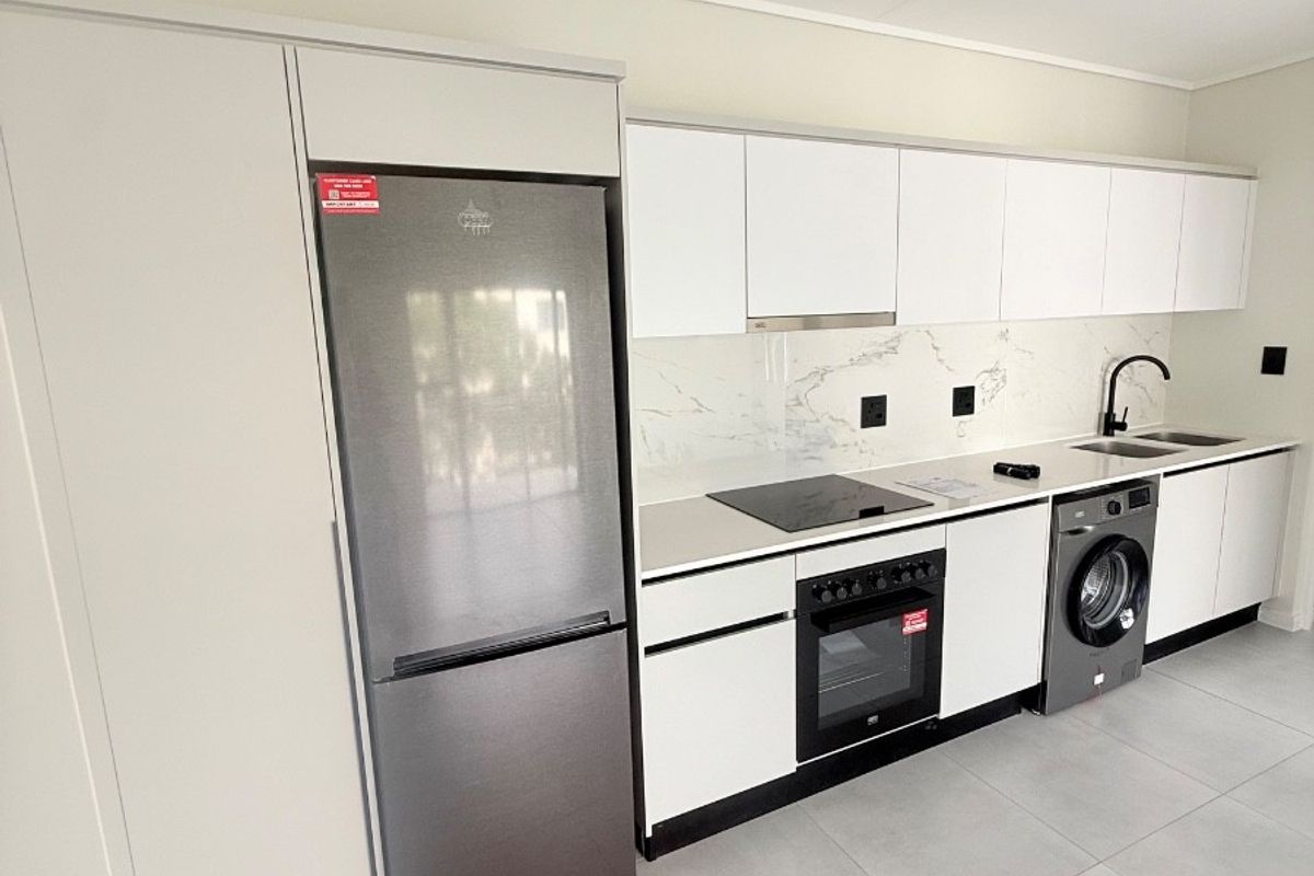 Modern kitchen featuring sleek white cabinetry, stone-look backsplash, integrated oven and hob, and contemporary black fixtures with neutral tiled flooring.