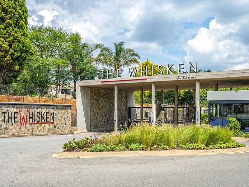 The main entrance and security gatehouse of The Whisken complex, featuring modern stone cladding, professional landscaping, and secure access control.