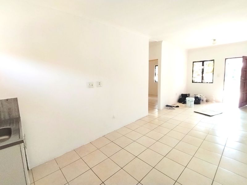 An empty open-plan living and kitchen area featuring neutral tiled flooring and direct access to the exterior.