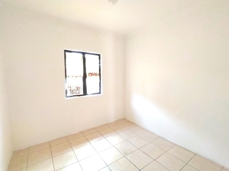 A simple, empty bedroom featuring neutral tiled flooring and a single window, providing a blank canvas for interior design.