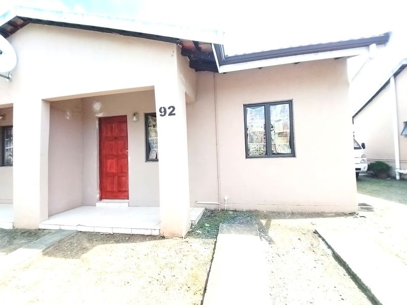 Front elevation of a single-story residential house featuring a tiled entrance porch, aluminum window frames, and a red timber front door.