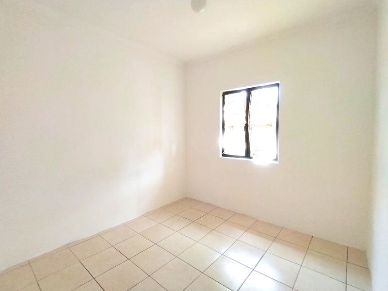 A bright, empty bedroom featuring neutral tiled flooring and a single casement window, providing a clean canvas for interior design.