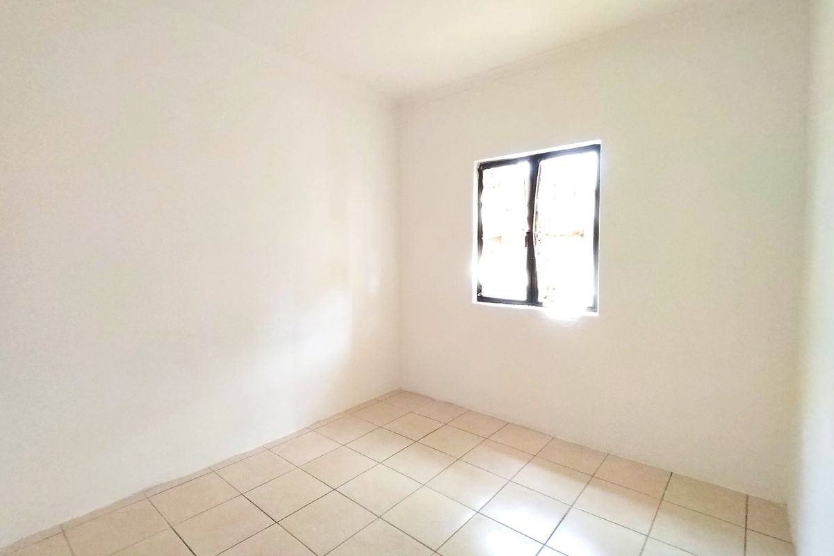 A bright, empty bedroom featuring neutral tiled flooring and a single casement window, providing a clean canvas for interior design.