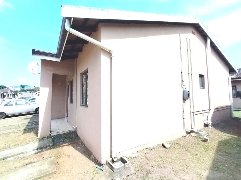 Side and rear view of the property showing exterior wall finishes, guttering, downpipes, and a small tiled entrance area.