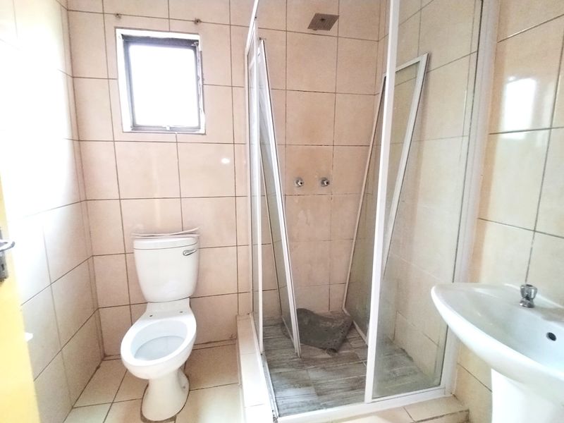 A functional bathroom featuring a pedestal basin, toilet, and a shower enclosure with tiled finishes throughout.