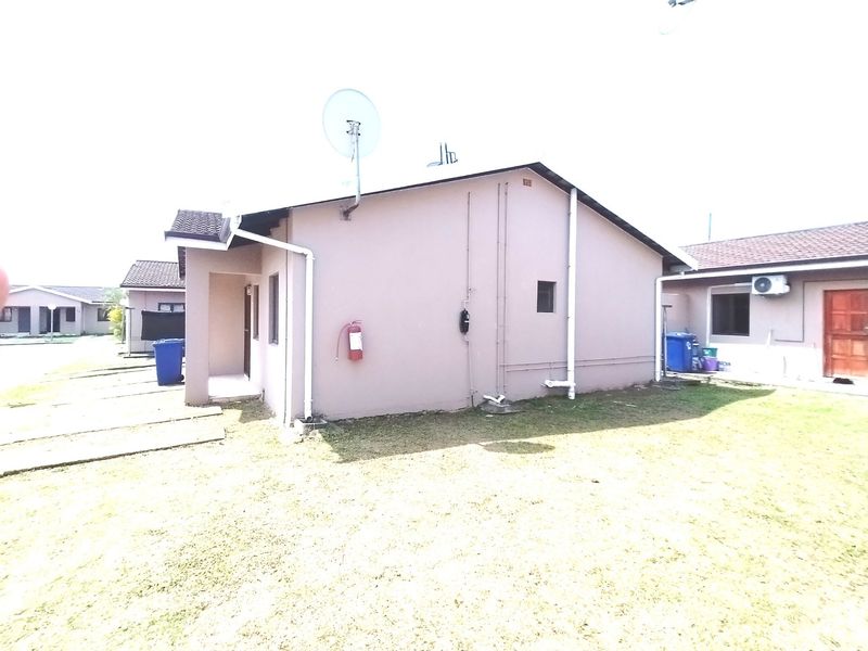 Rear exterior view of the property showing the side facade, lawn area, and fixed utility installations including plumbing and satellite dish.