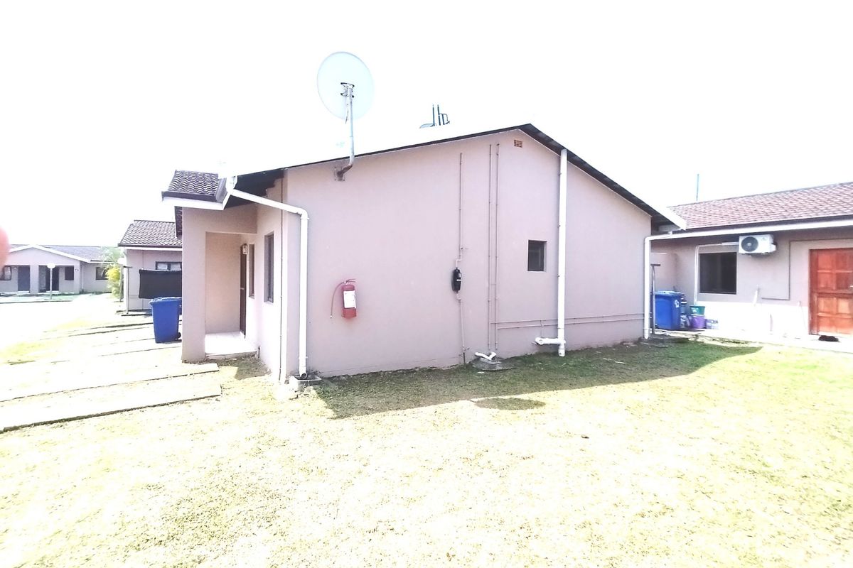 Rear exterior view of the property showing the side facade, lawn area, and fixed utility installations including plumbing and satellite dish.