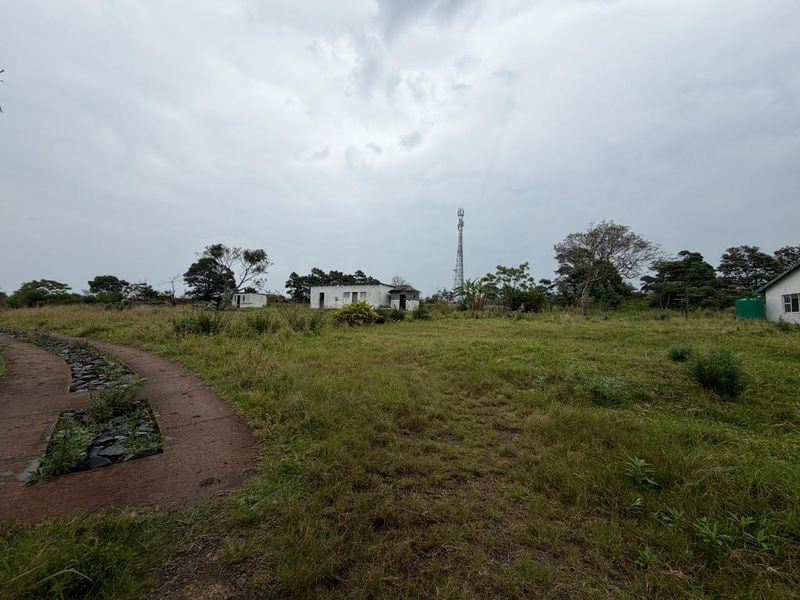 Expansive small holding grounds featuring a paved pathway, water tank, and distant view of a telecommunications mast on the property.