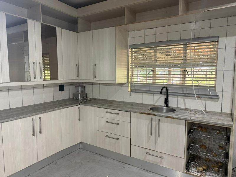 A functional kitchen featuring light wood-grain cabinetry, laminate countertops, a stainless steel sink, and tiled backsplash, currently in a vacant state.