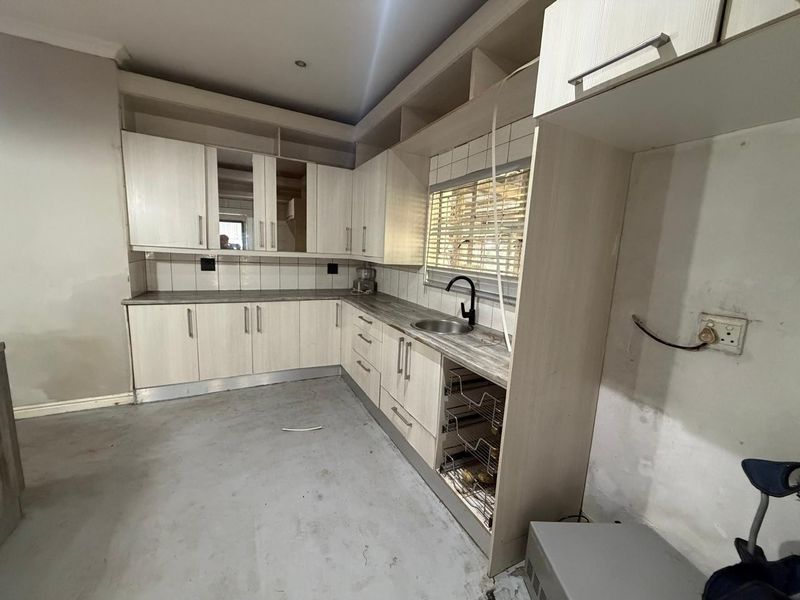 An unfinished kitchen space featuring light wood-look cabinetry, laminate countertops, and a stainless steel sink, requiring final wall finishes and flooring installation.
