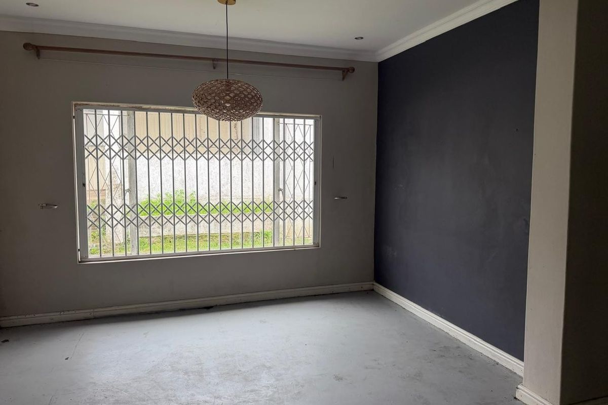 An empty living room featuring a dark accent wall, recessed downlighting, and a window fitted with a security gate.