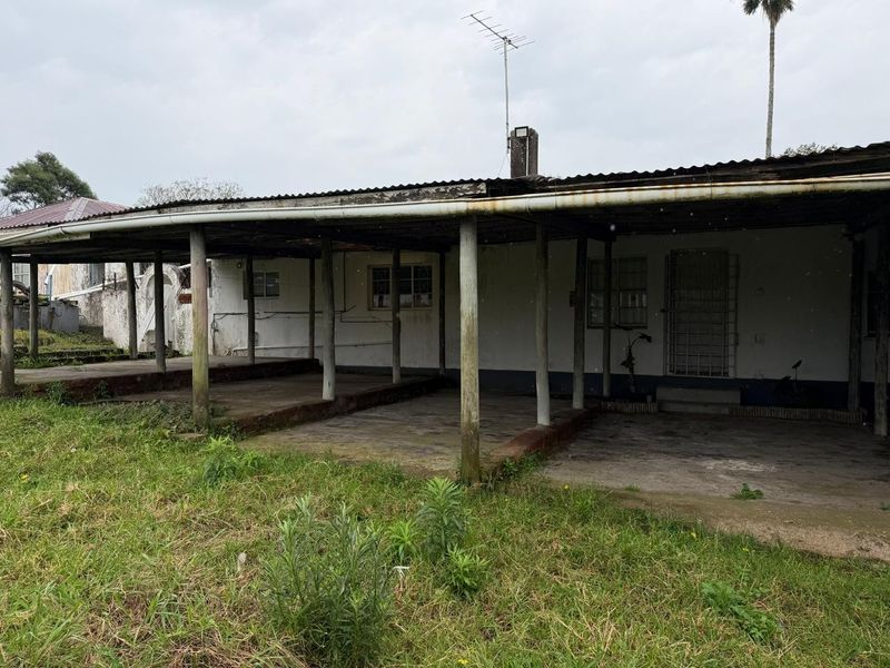 A rear exterior view of the property featuring a covered patio area with timber support posts and a corrugated iron roof structure.