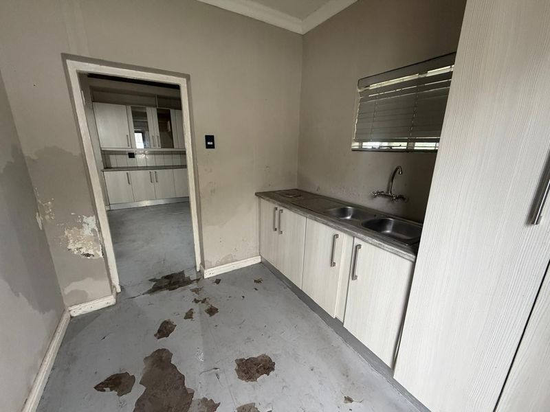 A functional scullery area featuring built-in cabinetry and a double basin sink, currently requiring cosmetic refurbishment and floor repairs.