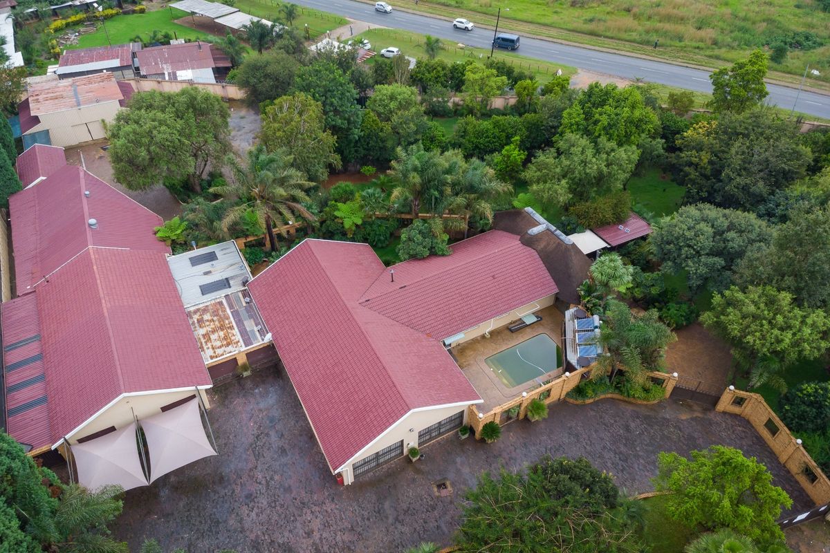 Aerial view of a farm property featuring multiple buildings with red metal roofing, a swimming pool, and extensive landscaped grounds.