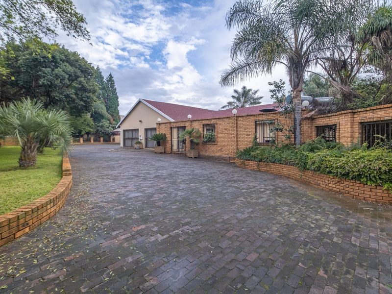 A spacious front exterior view of the farm property featuring a paved brick driveway, established garden, and a secure brick boundary wall.