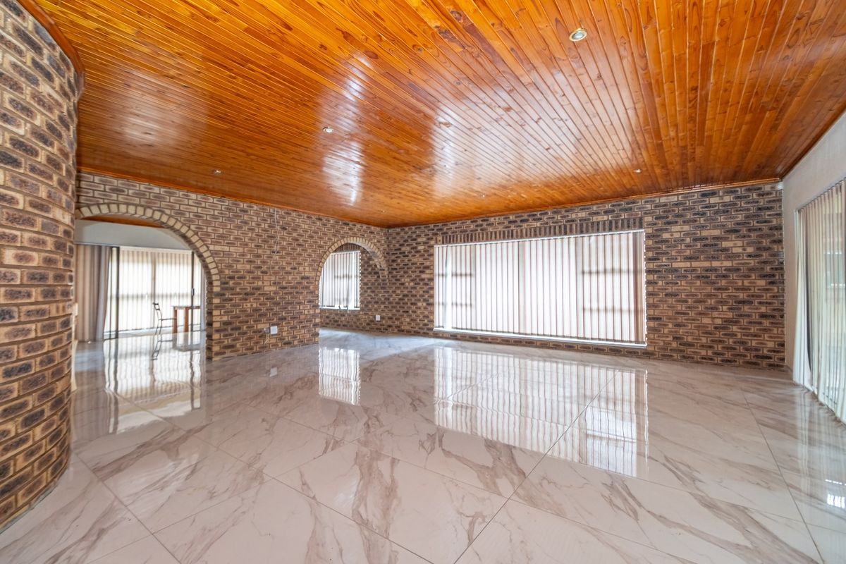 Spacious living area featuring polished marble-look floor tiles, exposed brick walls, and a warm timber tongue and groove ceiling with arched architectural details.