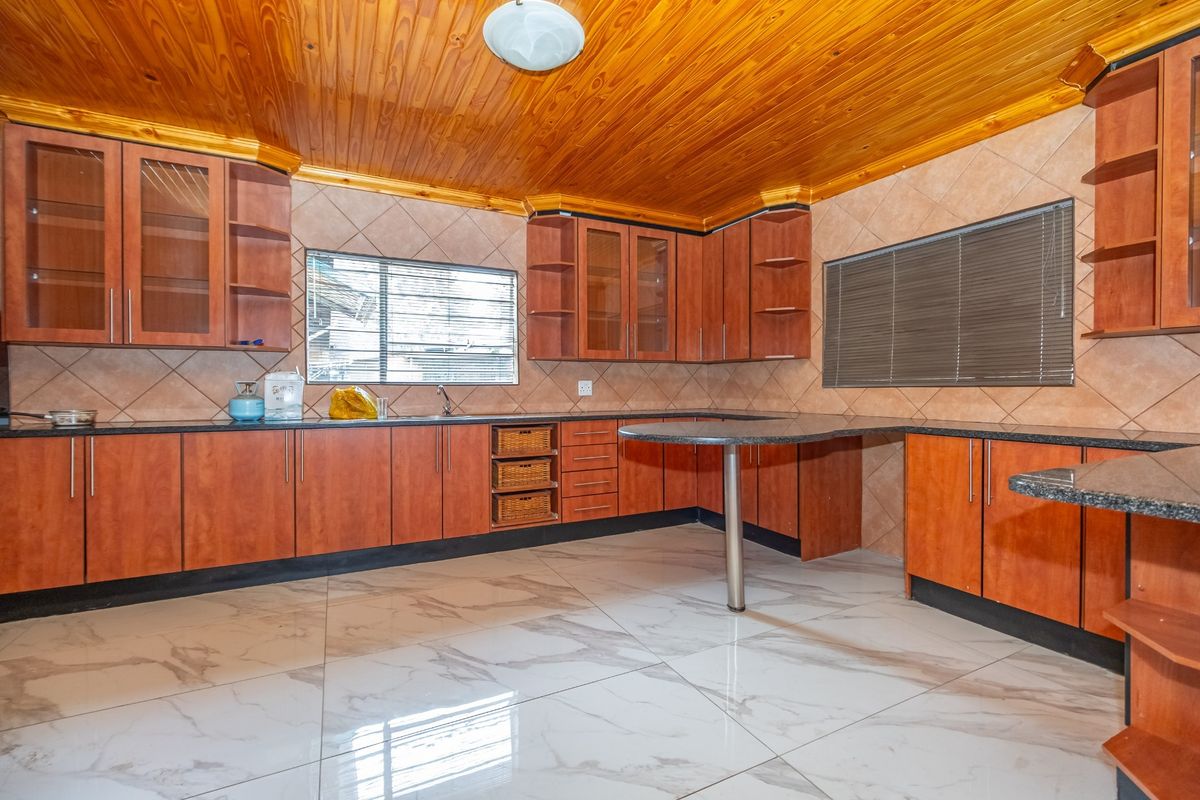 Spacious kitchen featuring wooden ceiling, granite countertops, ample built-in cabinetry, and modern marble-look floor tiles.